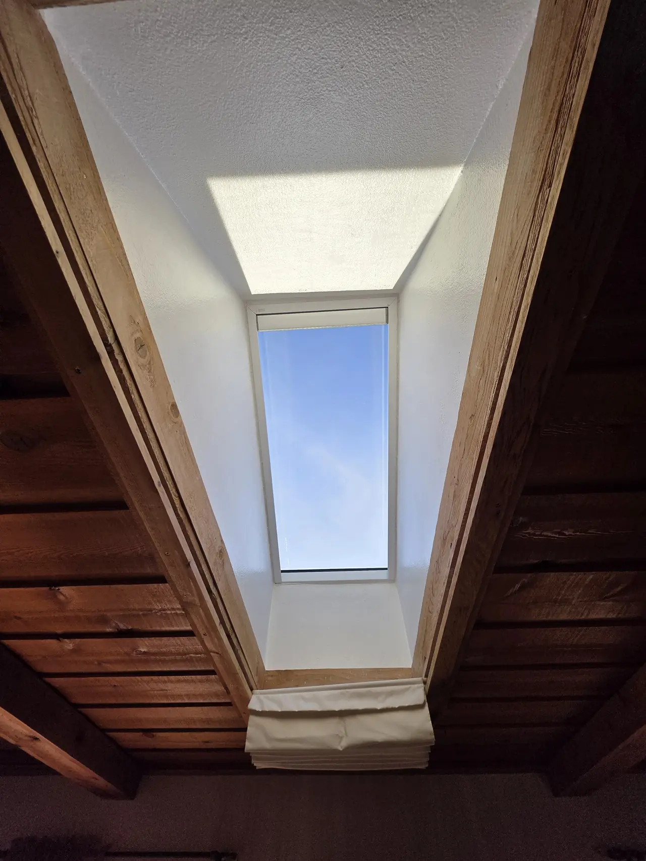 Bright white skylight shaft framed by a wood-beam ceiling